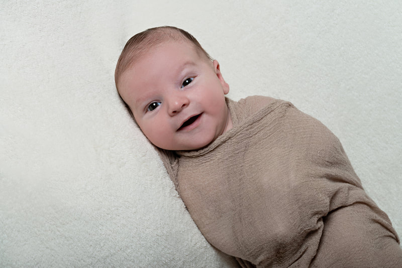 photo of a 6 week old infant baby boy in a beige cheesecloth wrap on a white fuzzy blanket