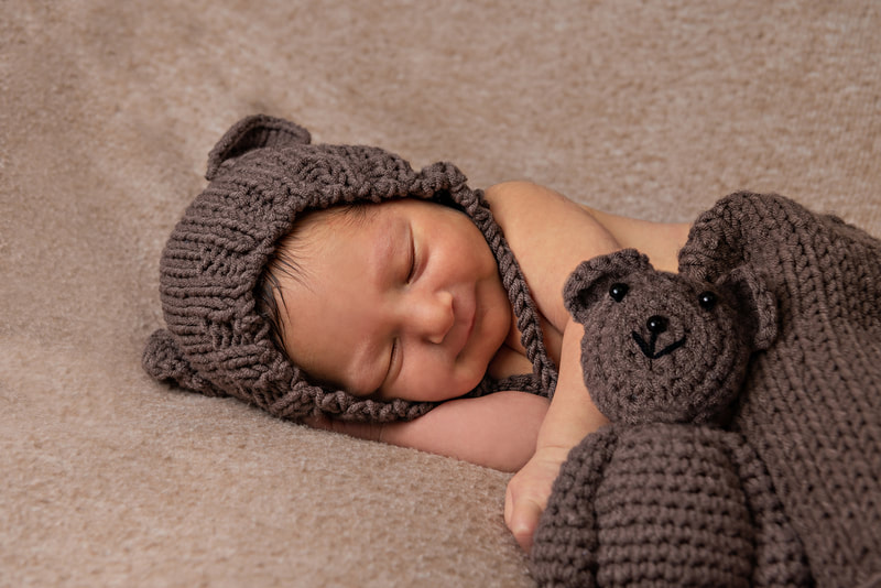 photo of a newborn baby boy dressed in a bear outfit with a knit teddy bear next to him