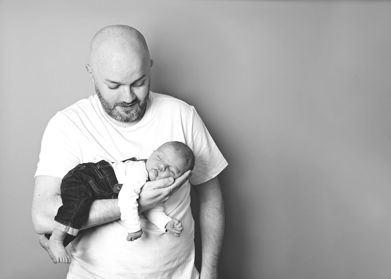 black and white photo of a dad holding his newborn baby boy while he looks down at him