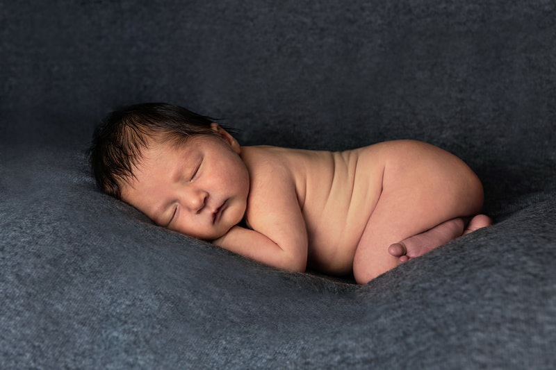 photo of a newborn baby boy curled up against a grey fabric background in a photo studio