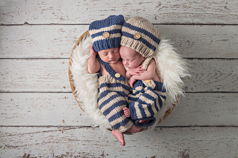 photo of twin newborn baby boys in coordinating blue and white knit outfits laying together in a basket with a white furry rug on top of a white wooden floor