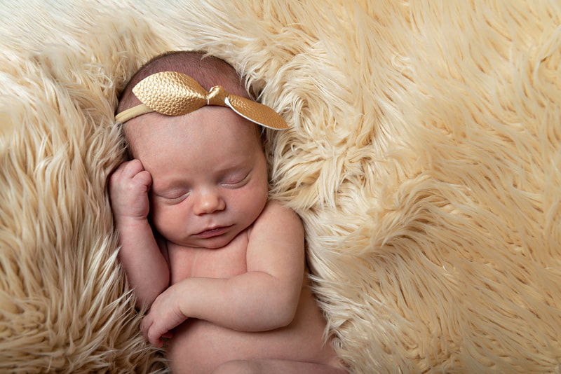 photo of a newborn baby girl with a faux leather gold headband laying on a beige furry rug