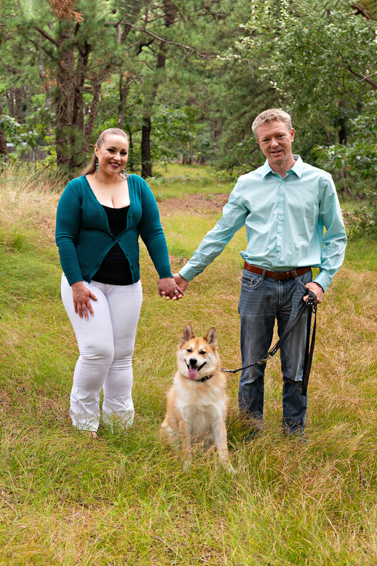 photo of a woman and a man holding hands above their dog, a husky pomeranian mix, who is sitting in between them